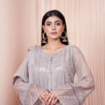 Elegant woman in pastel embroidered dress posing indoors with glamorous earrings.